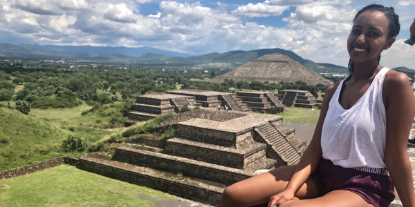A sitting woman smiles with large pyramids in the background